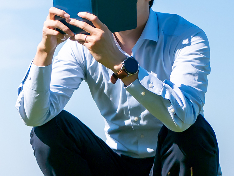 青空の下で本を読むビジネスマン